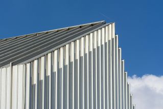 Low angle shot of a modern building with a corrugated steel facade against a clear blue sky.